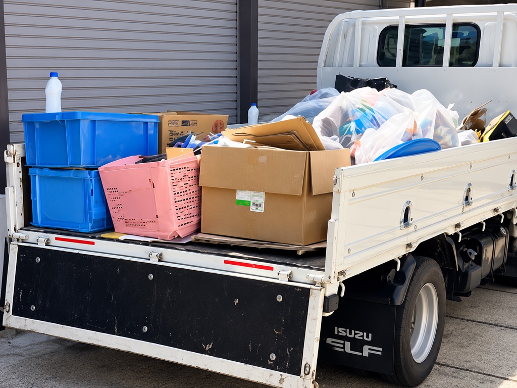 トラックの荷台に、収納ケースや段ボール、袋詰めした不用品を積み込んだ様子